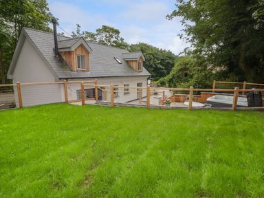 A house with a sloped roof a fenced grassy yard and a patio area with outdoor furniture and a hot tub at The Grove in Wolfsdale near Haverfordwest