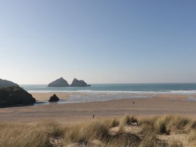 A beach with sand dunes in the foreground and rock formations in the sea Near Holywell Bay