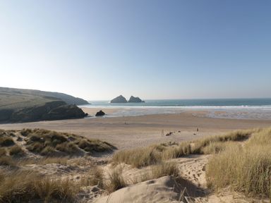 A sandy beach with grass-covered dunes and rocky cliffs by the sea at Horseshoe Cottage Near Holywell Bay