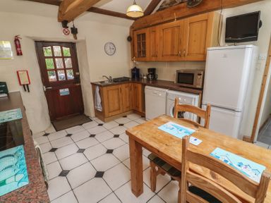A kitchen with wooden cabinets and appliances at Horseshoe Cottage Near Holywell Bay