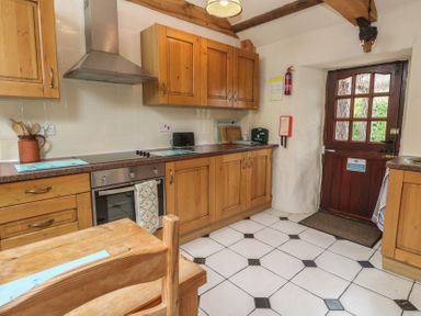 A kitchen with wooden cabinets and a door at Horseshoe Cottage near Holywell Bay