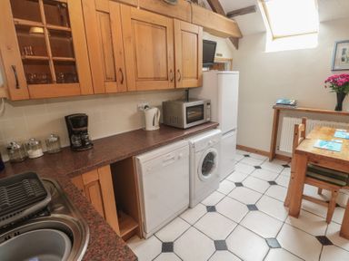 A kitchen with appliances and a dining table at Horseshoe Cottage near Holywell Bay