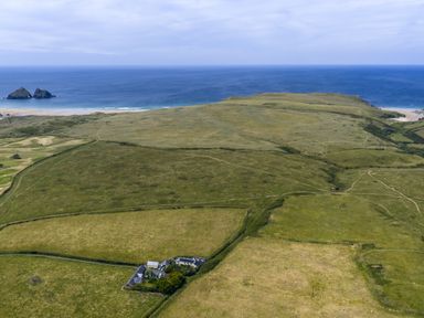 An aerial view of grassland and ocean at Horseshoe Cottage near Holywell Bay
