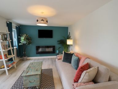 A living room with a sofa cushions a wooden coffee table a wall-mounted television and a fireplace at Villa Rose in Beadnell near Seahouses