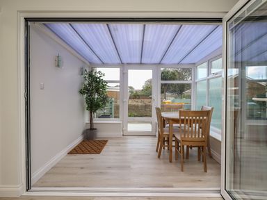 A dining area with a wooden table and four chairs a potted plant and glass doors at Villa Rose in Beadnell near Seahouses
