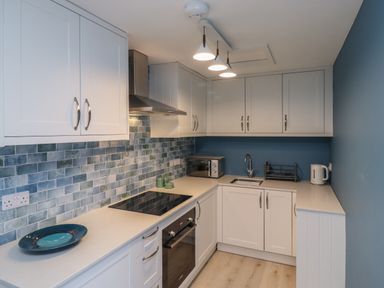 A kitchen with white cabinets blue tiled backsplash stove oven microwave sink and kettle at Villa Rose Beadnell near Seahouses