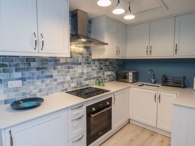 A kitchen with white cabinets blue tiled backsplash an oven and a sink at Villa Rose in Beadnell near Seahouses