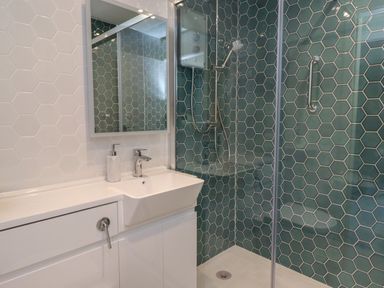 A bathroom with a white sink and cabinet next to a shower area with green hexagonal tiles at Villa Rose in Beadnell near Seahouses