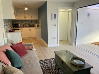 A living room with sofa and cushions small kitchen area and sliding glass door at Villa Rose in Beadnell near Seahouses