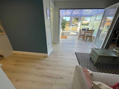 A room with a light wooden floor and a blue wall leading to a sunroom with a table and chairs at Villa Rose in Beadnell near Seahouses
