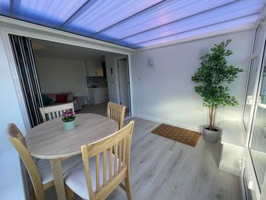 A dining area with a round wooden table and four chairs a potted plant mat on the floor and a visible kitchen and living space at Villa Rose in Beadnell near Seahouses