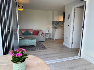 A living room with a sofa and cushions a wooden coffee table and a small kitchen area at Villa Rose Beadnell near Seahouses
