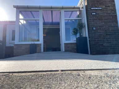A front porch with glass doors and windows a concrete pathway leading to the entrance with potted plants on either side at Villa Rose Beadnell near Seahouses