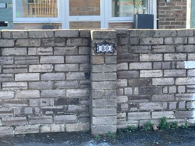 A brick wall with a house number 80 and a view of a door and window behind the wall at Villa Rose in Beadnell near Seahouses