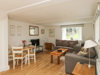 A living room with dining table, chairs, sofas, coffee table, TV, and window at Ixworth Cottage in Little Woodford near Ottery St Mary