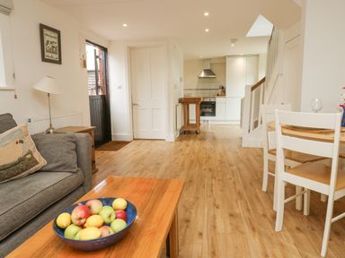 A living area with a bowl of fruit on a wooden coffee table and a kitchen in the background at Ixworth Cottage in Little Woodford near Ottery St Mary