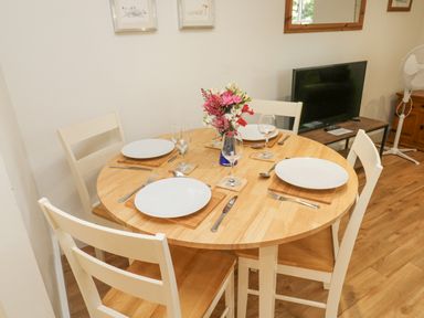 A dining area with a round wooden table set for four with plates glasses and cutlery at Ixworth Cottage in Little Woodford near Ottery St Mary