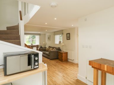 An open living space with a microwave on a wooden counter a staircase and sofas near windows at Ixworth Cottage in Little Woodford near Ottery St Mary