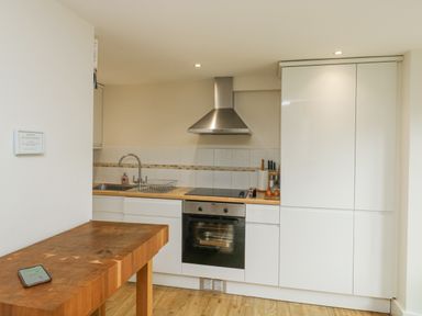 A kitchen with a wooden island table oven stovetop stainless steel hood and white cabinets at Ixworth Cottage in Little Woodford near Ottery St Mary
