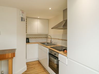 A kitchen with white cabinets a wooden countertop an oven a stovetop a sink a kettle and a cutting board at Ixworth Cottage in Little Woodford near Ottery St Mary