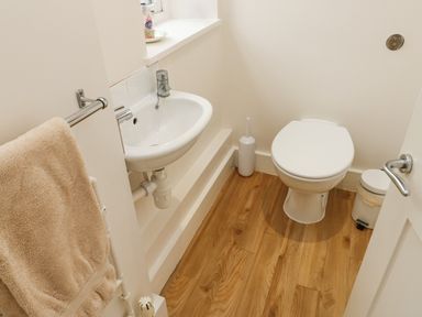 A small bathroom with a toilet sink towel and wooden floor at Ixworth Cottage in Little Woodford near Ottery St Mary