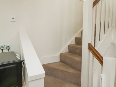 A carpeted staircase with white banisters and wooden handrail near a wall with a thermostat and power outlets at Ixworth Cottage in Little Woodford near Ottery St Mary