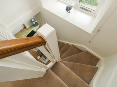 A carpeted staircase with a wooden handrail next to a window with a small bird decoration at Ixworth Cottage in Little Woodford near Ottery St Mary