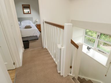 A hallway with staircase railing and a bedroom with a bed and nightstand at Ixworth Cottage in Little Woodford near Ottery St Mary