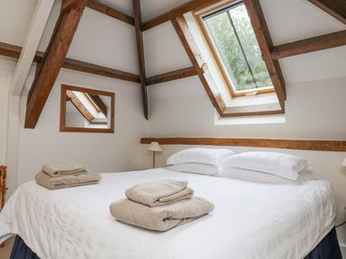 A bedroom with a double bed folded towels on bed skylight window and wooden beams at Ixworth Cottage in Little Woodford near Ottery St Mary