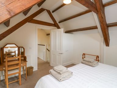 A bedroom with wooden ceiling beams a bed with folded towels a dressing table and an open door at Ixworth Cottage in Little Woodford near Ottery St Mary