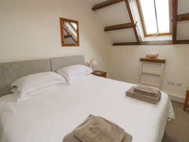 A bedroom with a double bed white bedding towels on the bed a wooden framed mirror lamp on a bedside table and a skylight window at Ixworth Cottage Little Woodford near Ottery St Mary