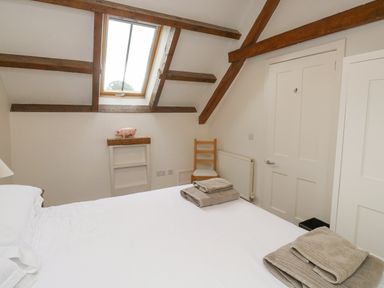 A bedroom with a bed towels a wooden chair skylight window and wooden beams at Ixworth Cottage in Little Woodford near Ottery St Mary