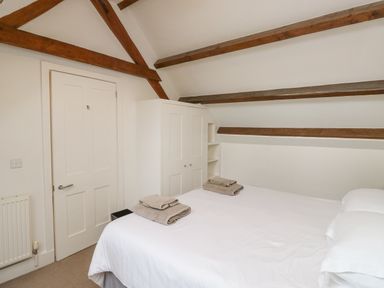 A bedroom with a double bed with white bedding towels on the bed a white wardrobe and wooden ceiling beams at Ixworth Cottage in Little Woodford near Ottery St Mary
