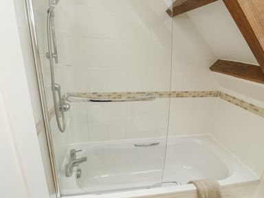 A bathroom with a bathtub shower combination tiled walls and wooden beams at Ixworth Cottage Little Woodford near Ottery St Mary