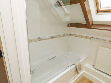 A bathroom with a bathtub and glass shower screen under a skylight window with wooden beams at Ixworth Cottage in Little Woodford near Ottery St Mary