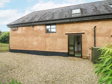 A gravel yard outside a building with a window and a glass door at Ixworth Cottage in Little Woodford near Ottery St Mary