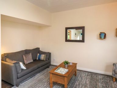 A living room with a gray sofa pillows a wooden coffee table with a plant a wall mirror and a small bookshelf at Ramson in Saltburn-By-The-Sea