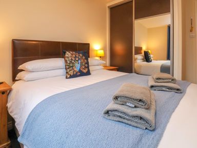 A bedroom with a bed folded towels a peacock cushion bedside tables and a lamp at Ramson in Saltburn-By-The-Sea