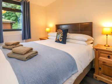 A bedroom with a bed made with white sheets blue blanket and folded towels two bedside tables with lamps and a window with blue curtains at Ramson in Saltburn-By-The-Sea