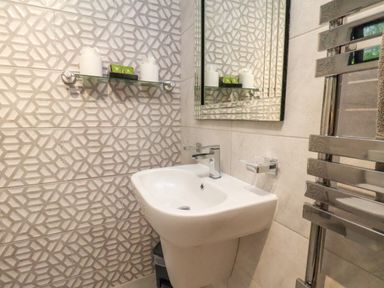 A bathroom sink with a modern faucet a wall-mounted mirror a shelf holding toiletries and towels and a chrome towel radiator at Ramson in Saltburn-By-The-Sea