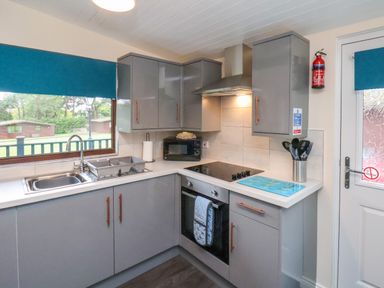 A kitchen with grey cabinets a window with a blue blind a sink stove oven microwave and kitchen utensils at Ramson in Saltburn-By-The-Sea