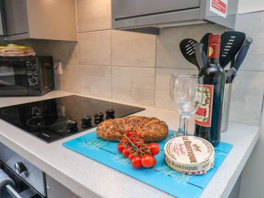 A kitchen counter with a loaf of bread cherry tomatoes cheese bottle of wine two wine glasses and kitchen utensils at Ramson in Saltburn-By-The-Sea