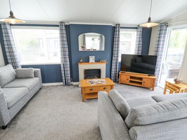 A living room with grey sofas a wooden coffee table and television at Sunset Lodge in Woodhall Spa