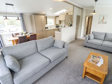 A living room with two grey sofas a wooden coffee table and an open kitchen with a dining table at Sunset Lodge in Woodhall Spa