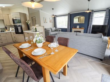 An open plan kitchen and living room with a wooden dining table set with plates and glasses at Sunset Lodge in Woodhall Spa
