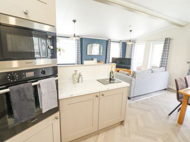 A kitchen with built in ovens and a counter overlooking a living room with a sofa and TV at Sunset Lodge in Woodhall Spa