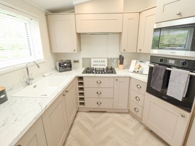 A kitchen with beige cabinets a marble countertop a gas stove an oven a toaster a knife block and a sink at Sunset Lodge in Woodhall Spa