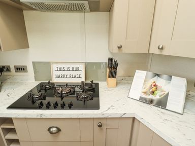 A kitchen countertop with a gas stove a knife block an open cookbook and a sign that reads this is our happy place at Sunset Lodge in Woodhall Spa