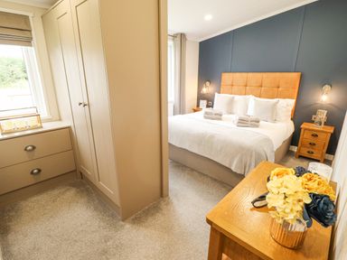 A bedroom with a bed a headboard bedside tables and flowers on a table at Sunset Lodge in Woodhall Spa