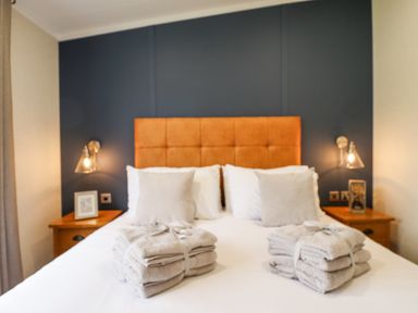 A bedroom with a bed with an orange headboard towels on the bed and bedside tables with lamps at Sunset Lodge in Woodhall Spa